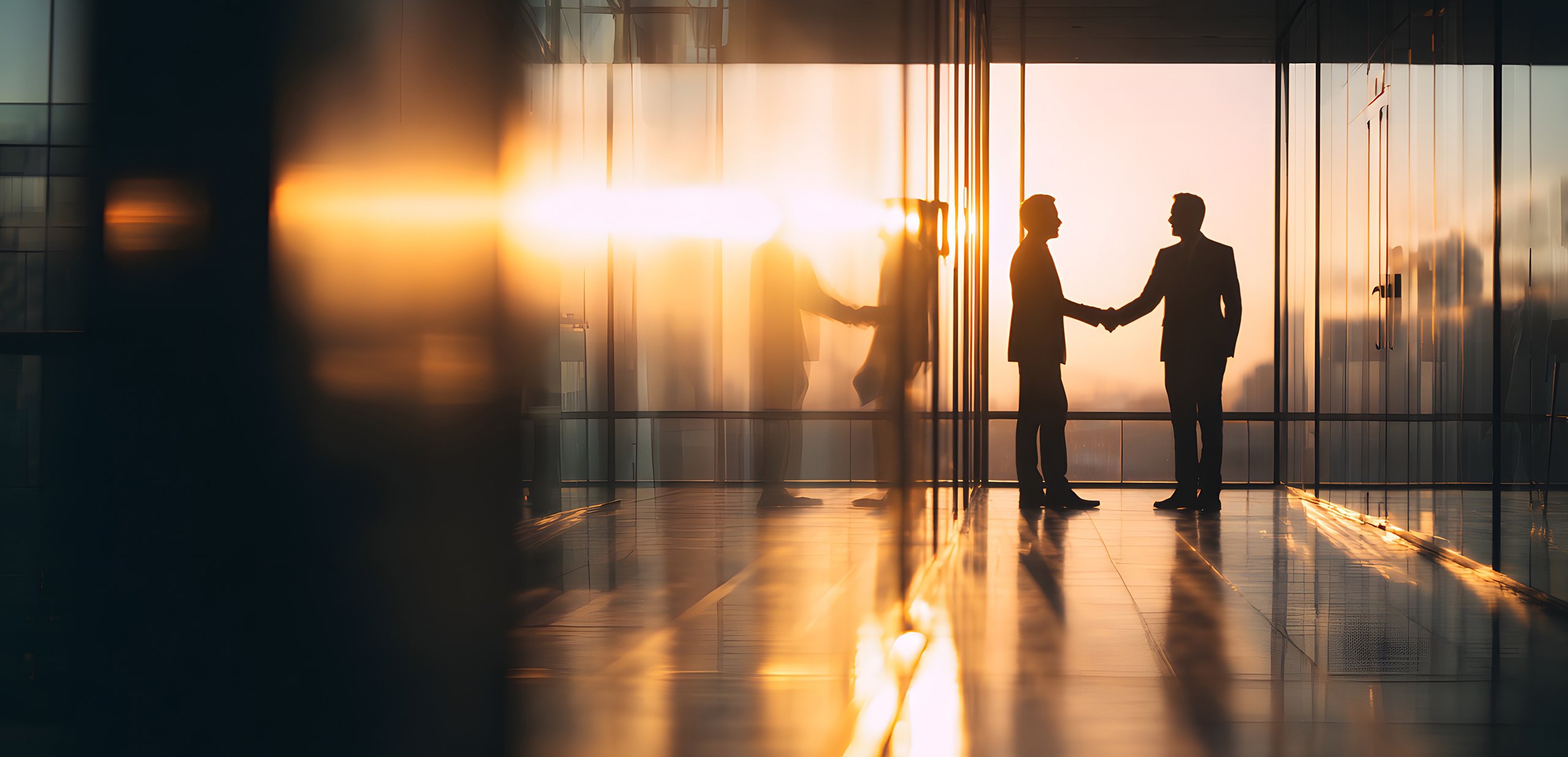 Silhouetten von zwei Geschäftspartnern, die sich bei Sonnenuntergang im hellen, modernen Büro die Hand geben – symbolisiert eine erfolgreiche Franchise-Partnerschaft.